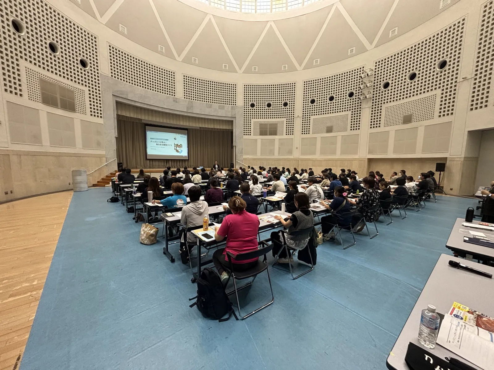ドーム天井の円形ホールいっぱいに着席した受講者と、舞台上で話す川崎真衣